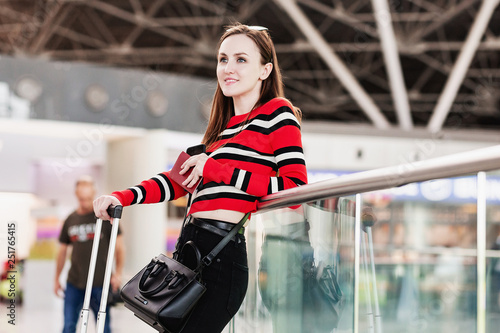 Pretty young woman chats in a smartphone with her friends waiting for a flight at the airport are standing next to their luggage. Meeting expectation concept