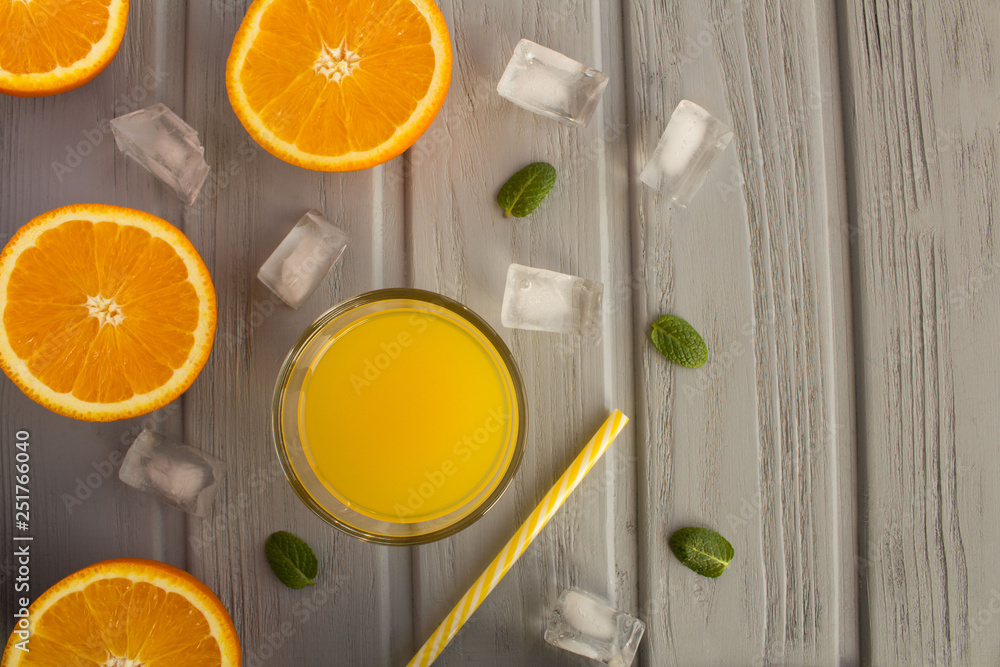 Orange juice in the glass and halves of oranges on the grey wooden background.Top view.Copy space. Orange juice in the glass and halves of oranges on the grey wooden background.Top view.Copy space.
