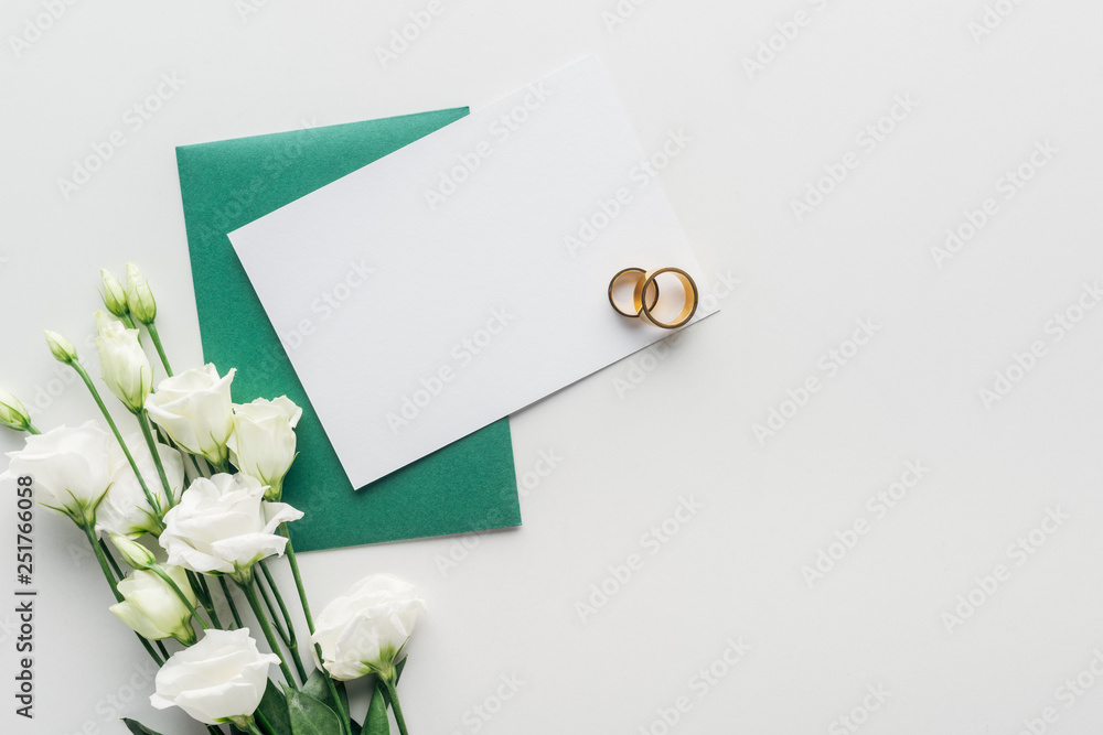 top view of empty card with green envelope, flowers and golden wedding rings on grey background top view of empty card with green envelope, flowers and golden wedding rings on grey background