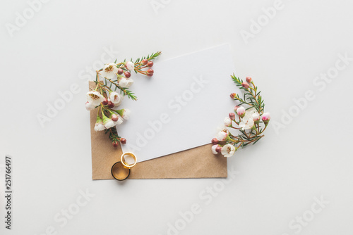 top view of empty card with brown envelope, flowers and wedding rings on grey background photo