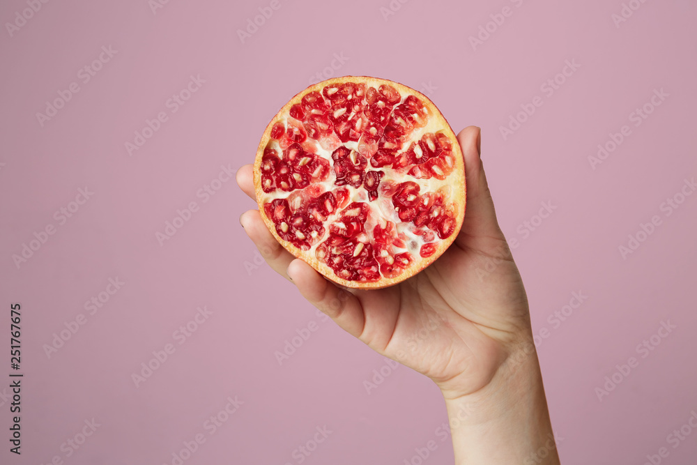 Hands of a young woman holding a red pomegranate. healthy food concept over pink background Hands of a young woman holding a red pomegranate. healthy food concept over pink background