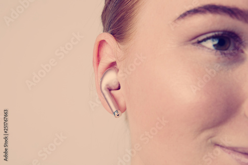 Close-up portrait of charming redhead caucasian woman with happy smile listening music with wireless earphone in ear