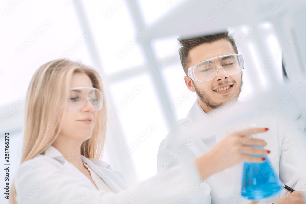 smiling scientist showing his colleague a flask of liquid.