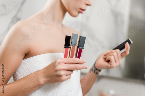 Young woman chosing lipstick from various colors wrapped in towels in the bathroom. beauty makeup and skincare concept