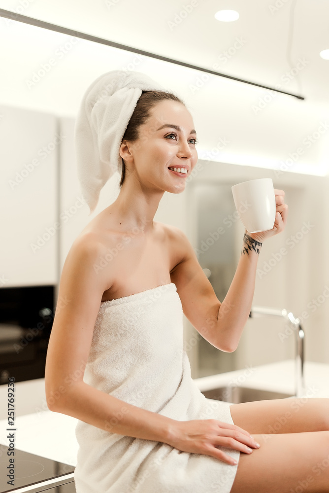 Beautiful young woman wrapped in towels waking in the morning drinking from a cup in modern kitchen. lifestyle concept Beautiful young woman wrapped in towels waking in the morning drinking from a cup in modern kitchen. lifestyle concept