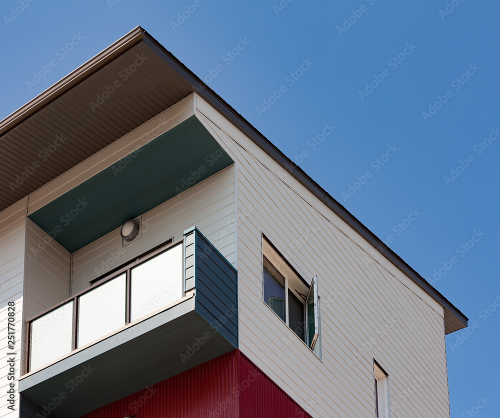 Upper storey detail of contemporary apartment condo building with balcony under blue sky