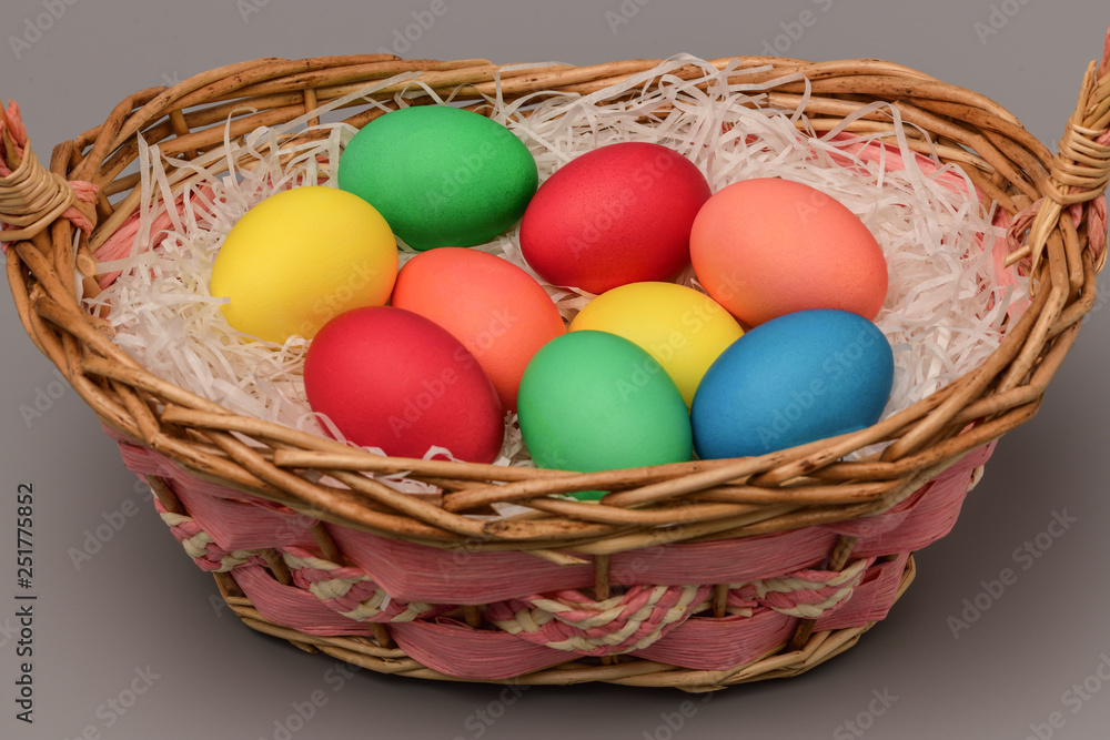 Easter colored eggs lie in a wicker basket on a gray background. Easter. Horizontal photography.