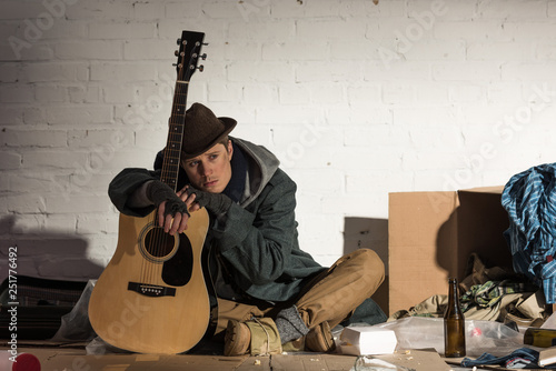 depressed homeless man leaning on guitar while sitting on street rubbish dump photo