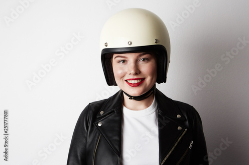 Handsome woman wearing black leather jacket and white moto helmet over background. Fashion, glamour and moto wear concept © KleverLevel