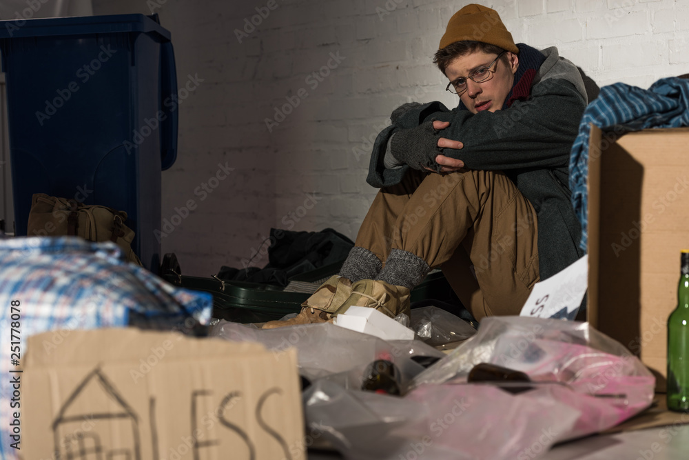 selective focus of depresses homeless man sitting by brick wall on rubbish dump selective focus of depresses homeless man sitting by brick wall on rubbish dump