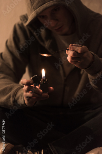 selective focus of addict man boiling heroin in spoon on lighter