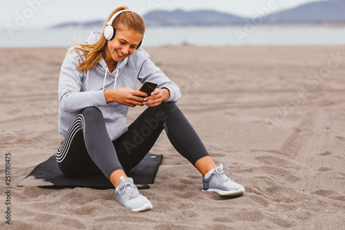Young sports woman listens to music on the beach