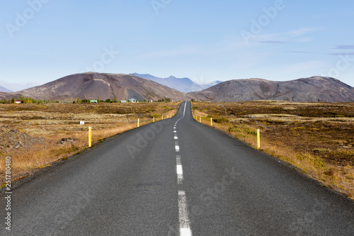 Paved road in barren volcanic landscape leading to distant mountain range in Golden Circle Region, Iceland, IS, Europe