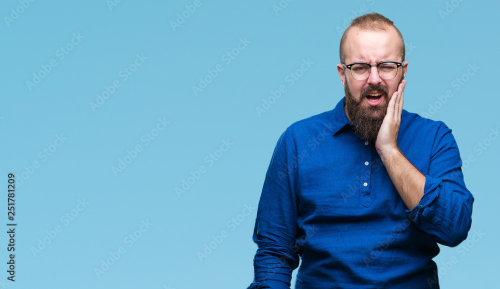 Young caucasian hipster man wearing glasses over isolated background touching mouth with hand with painful expression because of toothache or dental illness on teeth. Dentist concept. Young caucasian hipster man wearing glasses over isolated background touching mouth with hand with painful expression because of toothache or dental illness on teeth. Dentist concept.