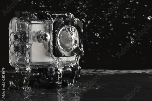 Flowing water on the waterproof action camera on wet black stone background 