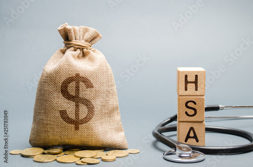 Wooden blocks with the word HSA and money bag with stethoscope. Health savings account. Health care. Health insurance. Investments. Tax-free medical expenses. Coins and dollar sign