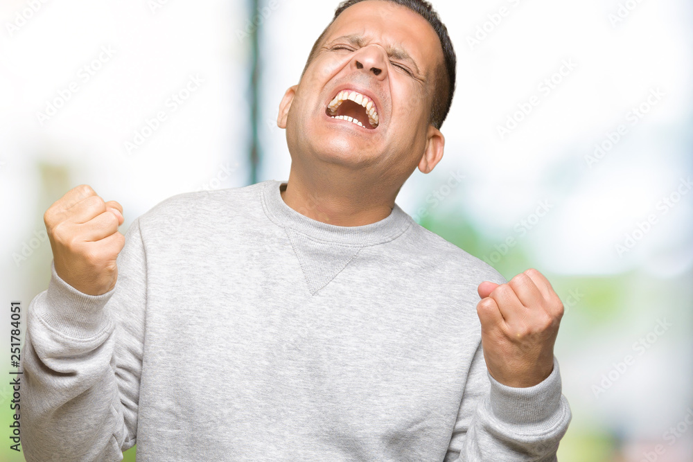 Middle age arab man wearing sport sweatshirt over isolated background very happy and excited doing winner gesture with arms raised, smiling and screaming for success. Celebration concept. Middle age arab man wearing sport sweatshirt over isolated background very happy and excited doing winner gesture with arms raised, smiling and screaming for success. Celebration concept.