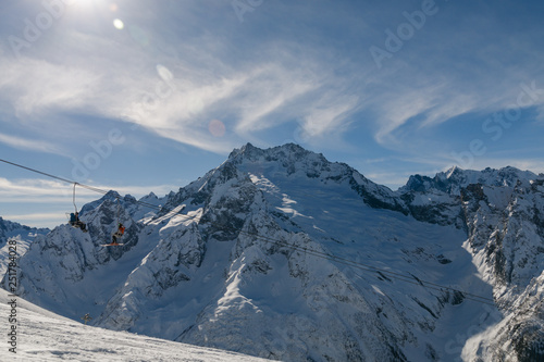 Skiers and snowboarders on the chair lift against the background of the Caucasus Mountains.