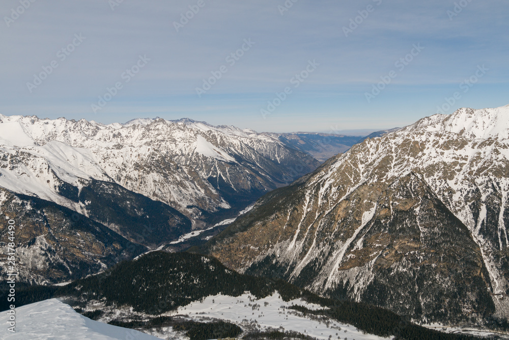 Snow-covered mountains and a valley without snow. Dombai, Caucasus, Karachay-Cherkessia, Russia.
