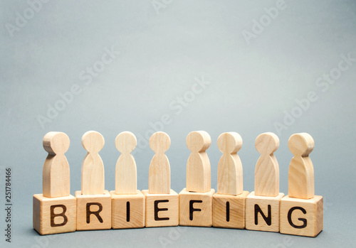 Wooden blocks with the word Briefing and a crowd of employees. Short press conference informative. Meeting. Cooperation. Develop a business strategy. Experience exchange. Teamwork. Business planning