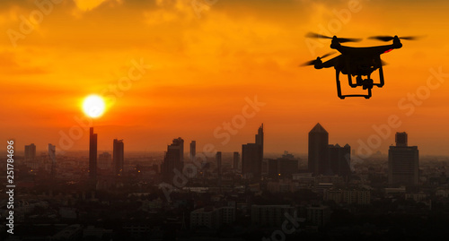 Silhouette of drone flying above city at sunset