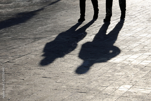 Fotografie People walking down the street, black silhouettes and shadows on pedestrian sidewalk