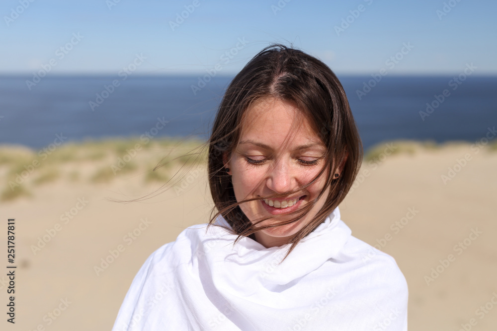 Beautiful dark hair young white european woman wrapped in white cloth with eyes closed and smiling. Happy. Close up. Shot on Parnidis dune in Nida, Lithuania, in Curonian Spit. Beautiful dark hair young white european woman wrapped in white cloth with eyes closed and smiling. Happy. Close up. Shot on Parnidis dune in Nida, Lithuania, in Curonian Spit.