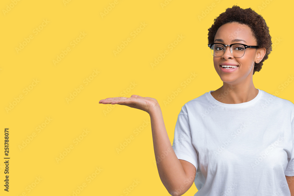 Beautiful young african american woman wearing glasses over isolated background smiling cheerful presenting and pointing with palm of hand looking at the camera. Beautiful young african american woman wearing glasses over isolated background smiling cheerful presenting and pointing with palm of hand looking at the camera.