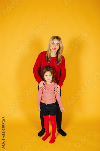 Mom and daughter standing on the yellow background in studio