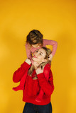 Happy little girl with her young mother on the yellow background. Daughter sitting on mom's neck. Smile