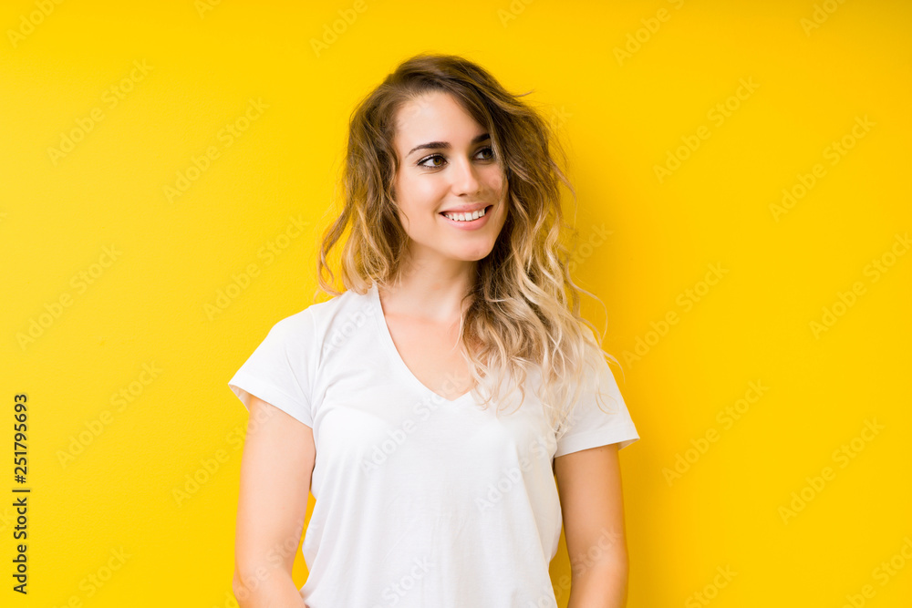 Young beautiful blonde woman over yellow background looking away to side with smile on face, natural expression. Laughing confident. Young beautiful blonde woman over yellow background looking away to side with smile on face, natural expression. Laughing confident.