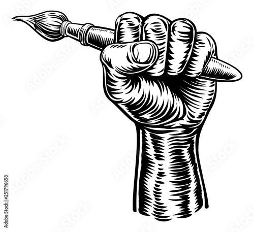 A fist hand holding an artists paintbrush in a vintage intaglio woodcut engraved or retro propaganda style