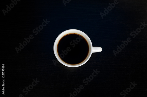 White cup of coffee on a black table, top view
