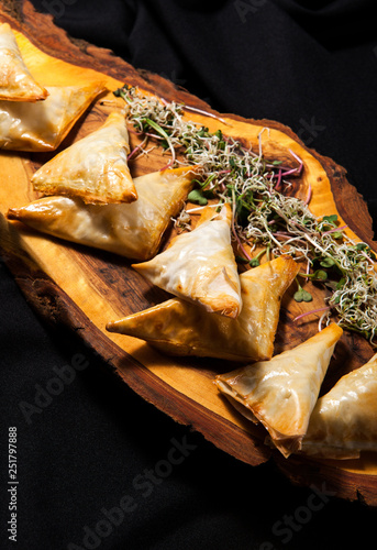 Phyllo pastry triangles on a wooden board on a dark background in close-up