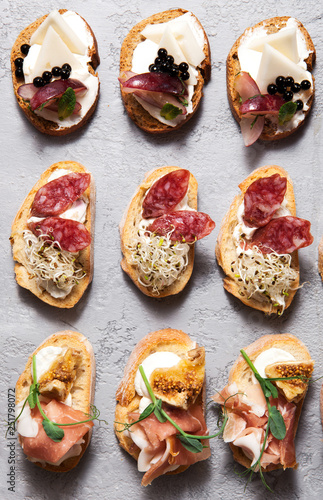 Different types of bruschetta with meat and cheese on a gray concrete background