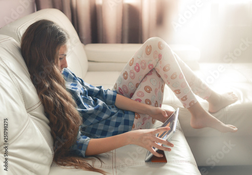 Teenage girl sitting at home with a tablet pc. Lifestyle image of beautiful Caucasian long-haired girl.