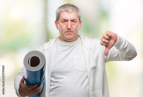 Handsome senior man holding yoga mat over isolated background with angry face, negative sign showing dislike with thumbs down, rejection concept