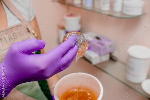 Wax bar with sugar paste depilation and beauty concept - sugar paste or wax honey for hair removing with bright  purple gloves hands of cosmetologist in spa salon. Top view several objects