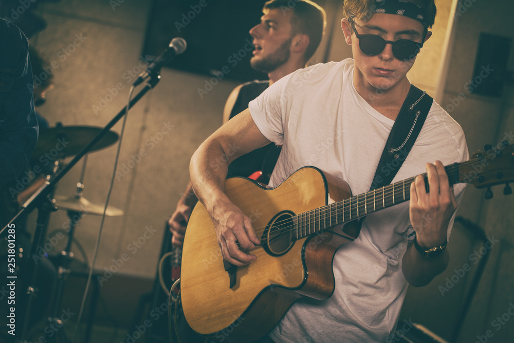 Hipster young man holding bass guitar and playing at repetition. Handsome  guitarist wearing in white t shirt, black spectacles and bandana. Another  member of band singing behind. Stock Photo | Adobe Stock
