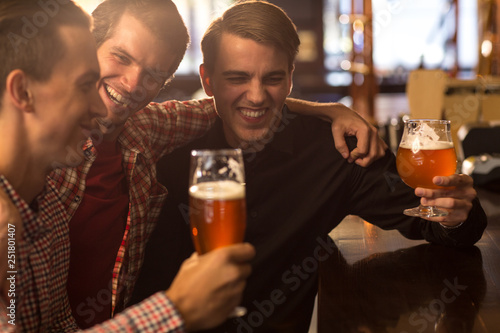 Friends hanging out together in bar. Cheerful and happy facial expressions of man laughing, having fun, communicating in bar. Men holding glasses of fresh, delicious beer.