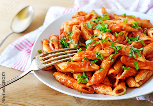 Delicious pasta dish with fresh basil on a wooden table. Top view scene, healthy eating or healthy lifestyle. Penne napoli or pasta arrabiata, closeup shot.