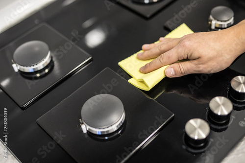 A woman hand with a yellow microfiber cloth rubs a glass ceramic stove in the kitchen.