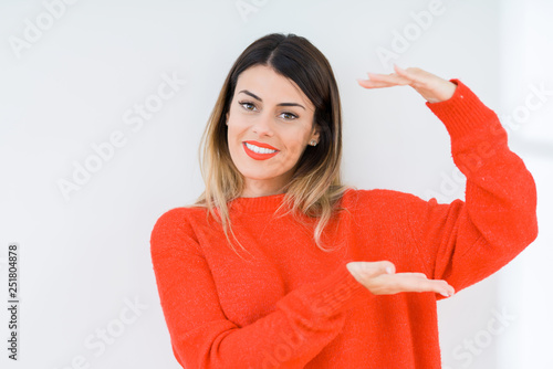 Young woman wearing casual red sweater over isolated background gesturing with hands showing big and large size sign, measure symbol. Smiling looking at the camera. Measuring concept. © Krakenimages.com
