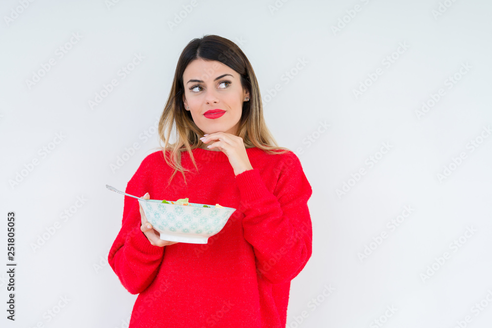Young woman eating fresh healthy salad over isolated background serious face thinking about question, very confused idea Young woman eating fresh healthy salad over isolated background serious face thinking about question, very confused idea