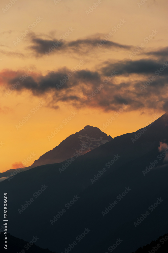 alpine landscape with peaks covered by snow and clouds. sunset