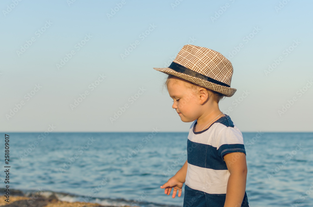 Little girl in a hat walks along the seashore