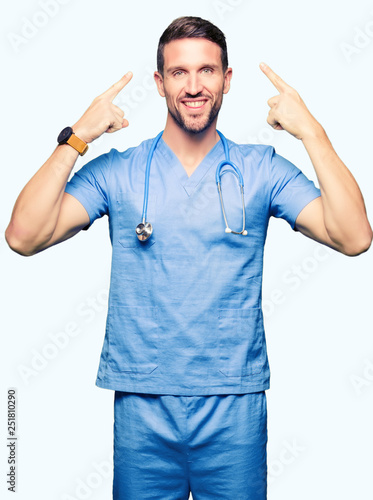 Handsome doctor man wearing medical uniform over isolated background Smiling pointing to head with both hands finger, great idea or thought, good memory