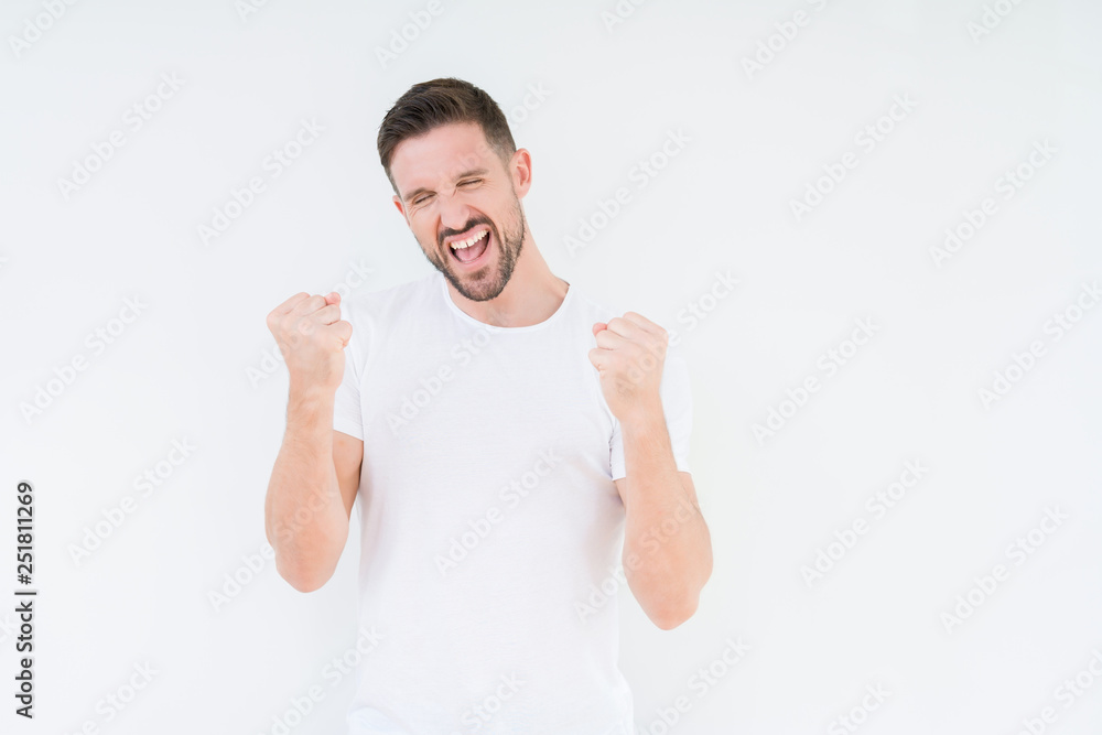 Young handsome man wearing casual white t-shirt over isolated background very happy and excited doing winner gesture with arms raised, smiling and screaming for success. Celebration concept. Young handsome man wearing casual white t-shirt over isolated background very happy and excited doing winner gesture with arms raised, smiling and screaming for success. Celebration concept.