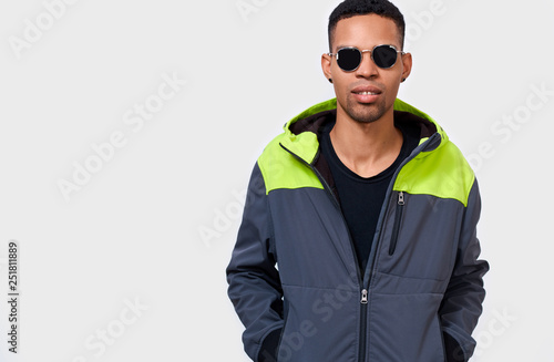 Stylish serious young African American man wearing round mirror sunglasses and sporty hoodie, looking to the camera and posing over white studio background. 