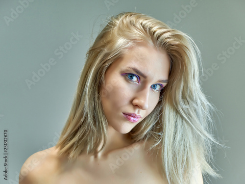 Closeup portrait concept of a beautiful blonde girl on a gray background. Hair develops in different directions.